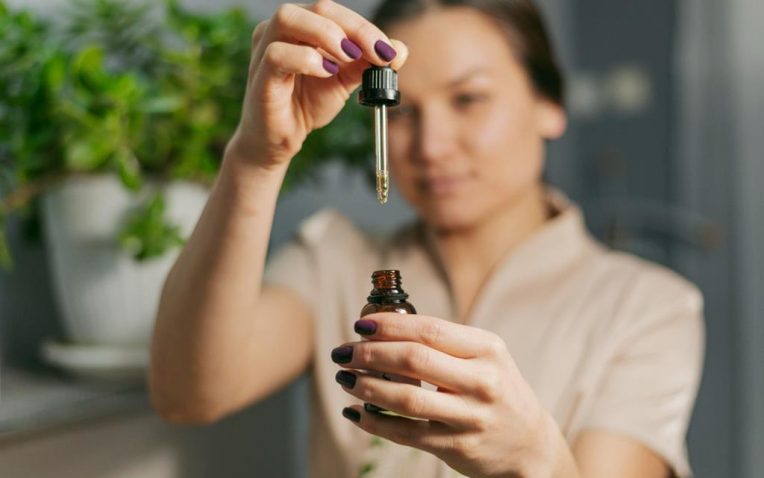 mulher segurando conta-gotas de um vidro de óleo essencial